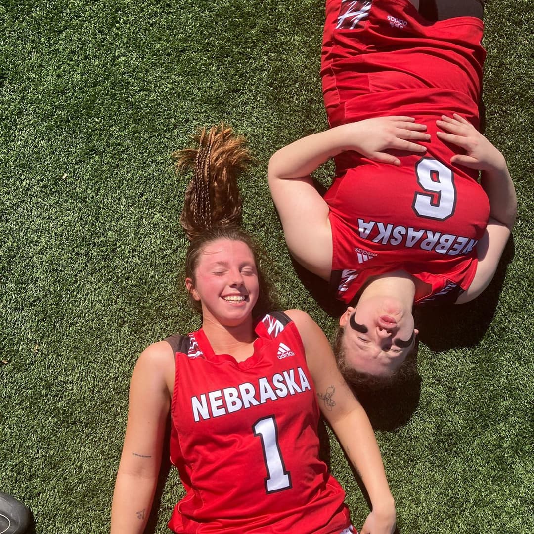 Overhead view of two students wearing Husker jerseys laying on the grass on a sunny day.